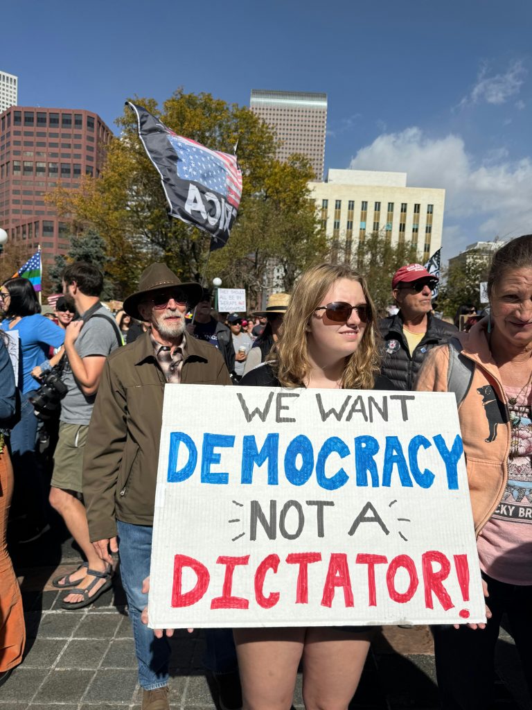A woman holds a sign saying "We Want Democracy, Not a Dictator!" at a protest. A sortition-based system could amplify her voice — and the voices of Americans everywhere. Photo by mana5280.