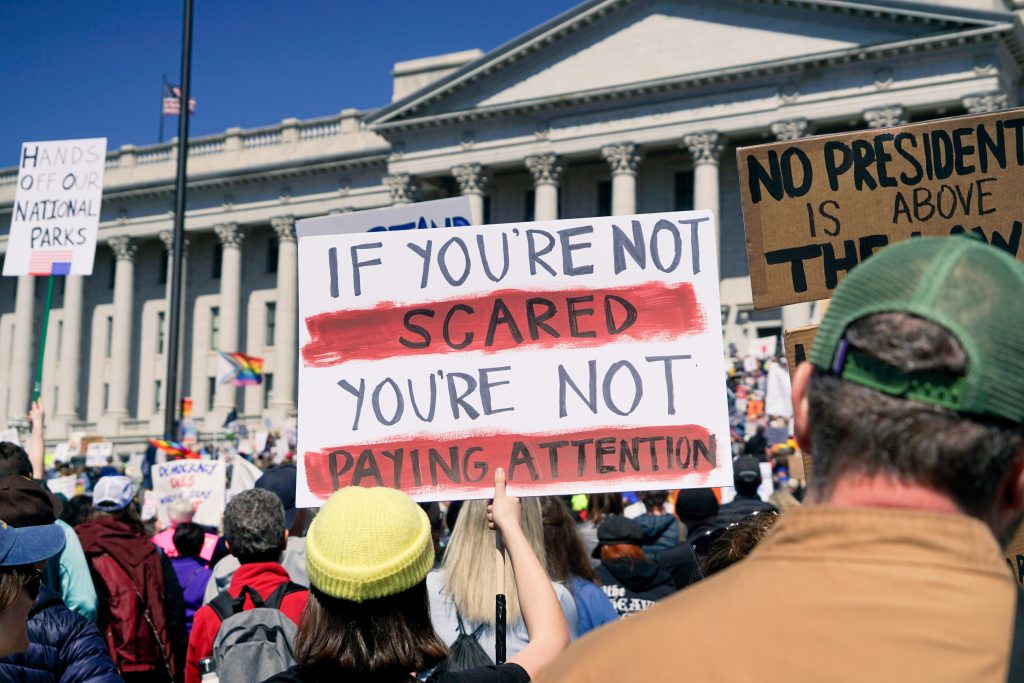 A sign protesting the actions of Donald Trump and Elon Musk being held up at the Hands Off protest outside the Utah State Capitol. Sortition could make the voice of everyday people, like these protestors, much louder. Photo by Mike Newbry.