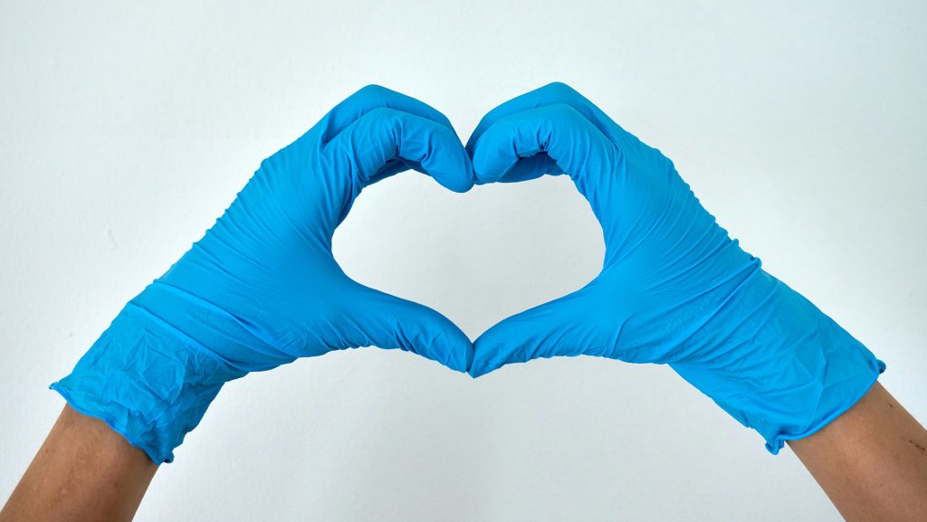 A person wearing medical gloves makes a heart with their hands. Holding big pharma accountable means putting people first. Photo by Anton on Unsplash.