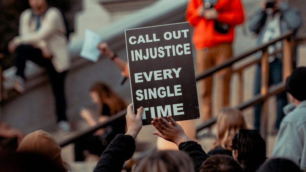 Someone holds up a sign calling out injustice during a protest. Photo by Colin Lloyd on Unsplash.